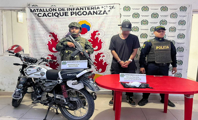 Do hombres de pie de Policía y Ejército y en la mitad un hombre capturado con camiseta negra y una moto al costado izquierdo
