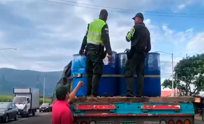 Dos policías encima de una tractomula con canecas azules y un ciudadano