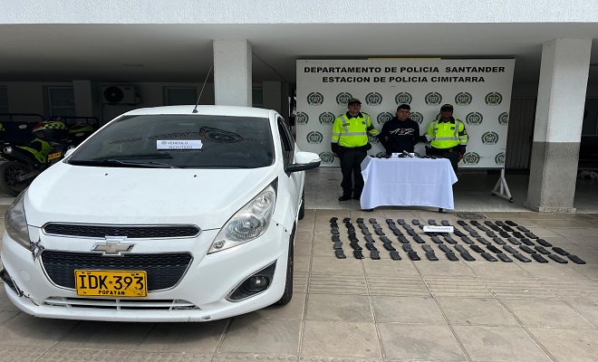 Exhibe el material incautado proveedores de armas, una pistola, y otros elementos. Al fondo, se observa el vehículo implicado en la incautación y una pancarta institucional de la Policía Nacional