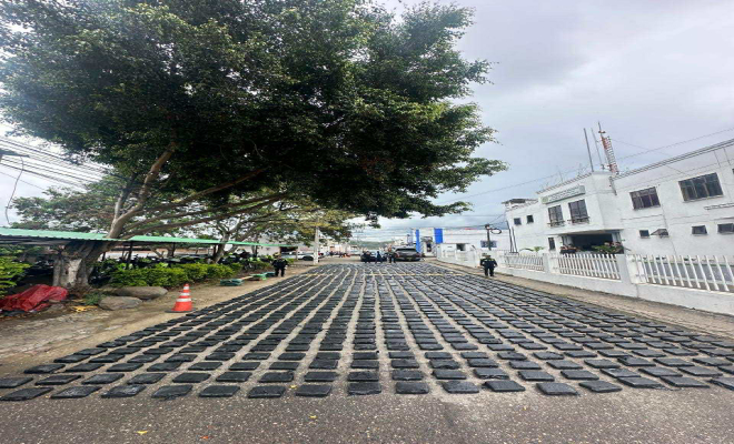 Persoa capturada al fondo, paquetes de marihuana en el piso organizados y patrullas de Policia alrededor 