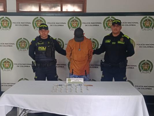 Hombre capturado con camiseta color naranja en medio de dos Polic&iacute;as