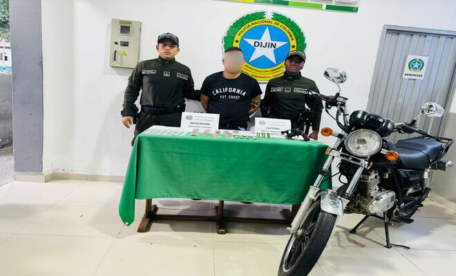 Dos funcionarios de la Polic&iacute;a Nacional presentan a una persona junto a una mesa con elementos incautados y una motocicleta.