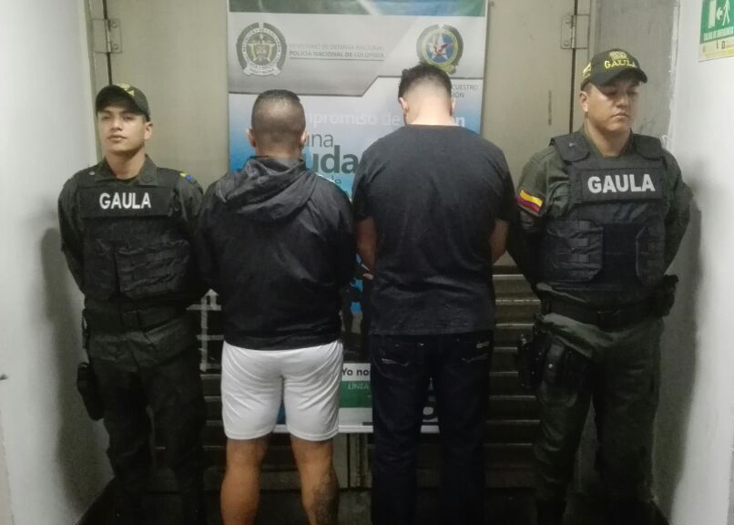 Dos personas capturadas son custodiadas por dos policías