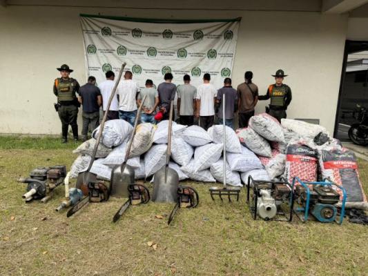 Dos Policías al lado de nueve personas y bultos de carbón con herramientas