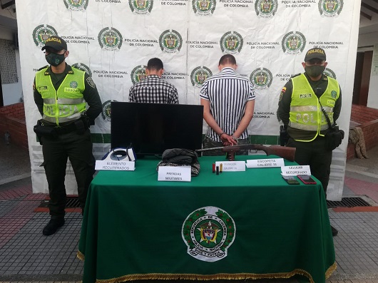 dos personas capturadas-policías custodiando-arma de fuego incautada